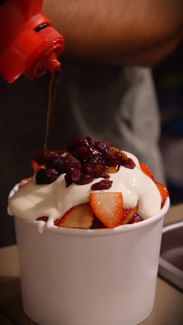 Chocolate cayendo sobre un vaso de fresas con crema